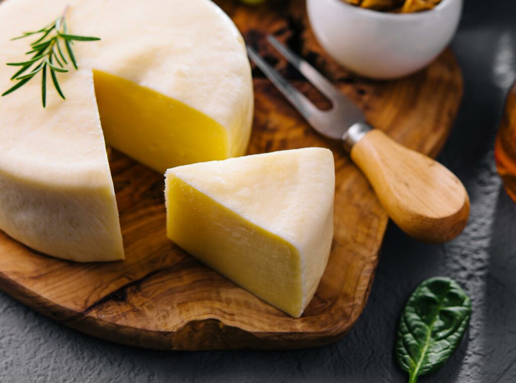 Queso artesanal redondo con una cuña cortada, adornado con romero, en una tabla de madera en Carnicería Rubio, Nules