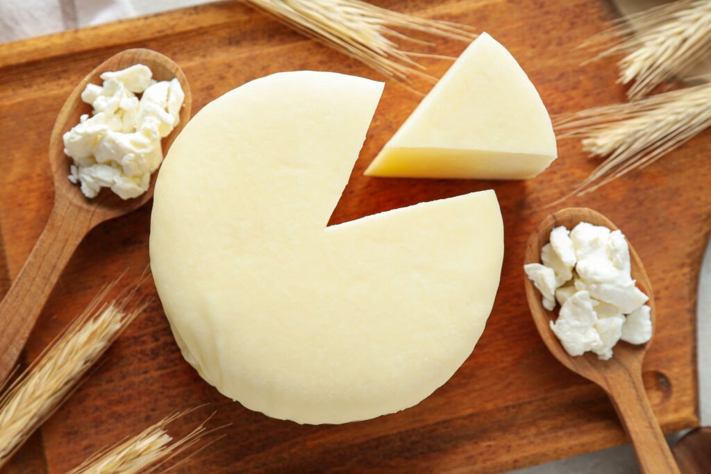 Queso fresco blanco redondo con una cuña cortada y cuajada en cucharas Quesos frescos y productos lácteos en la Carnicería Rubio en Nules