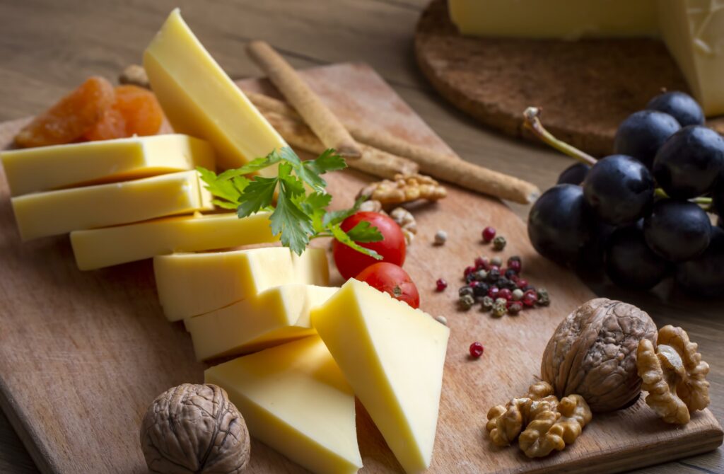 Tabla de quesos con lonchas y tacos, acompañada de uvas negras, nueces, tomatesados y nueces en una tabla redonda de madera, selección de Carnicería Rubio, Nules