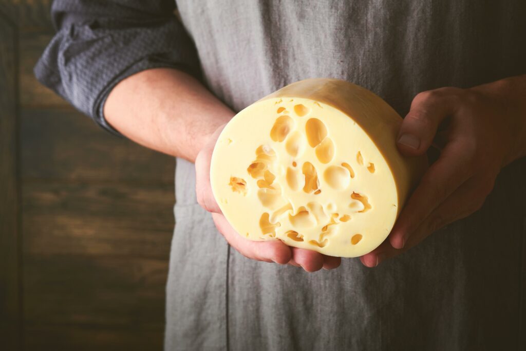 Hombre mostrando una gran pieza de queso tipo Emmental con agujeros, disponible en Carnicería Rubio, Nules